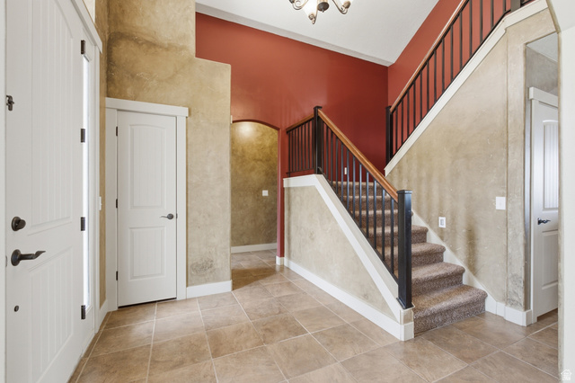 2567 West Rim Rock Drive Stockton, UT 84071 - Photo 7 of 64 Entryway featuring tile flooring, a carpeted staircase with dark iron balusters and wood handrail, and high ceilings