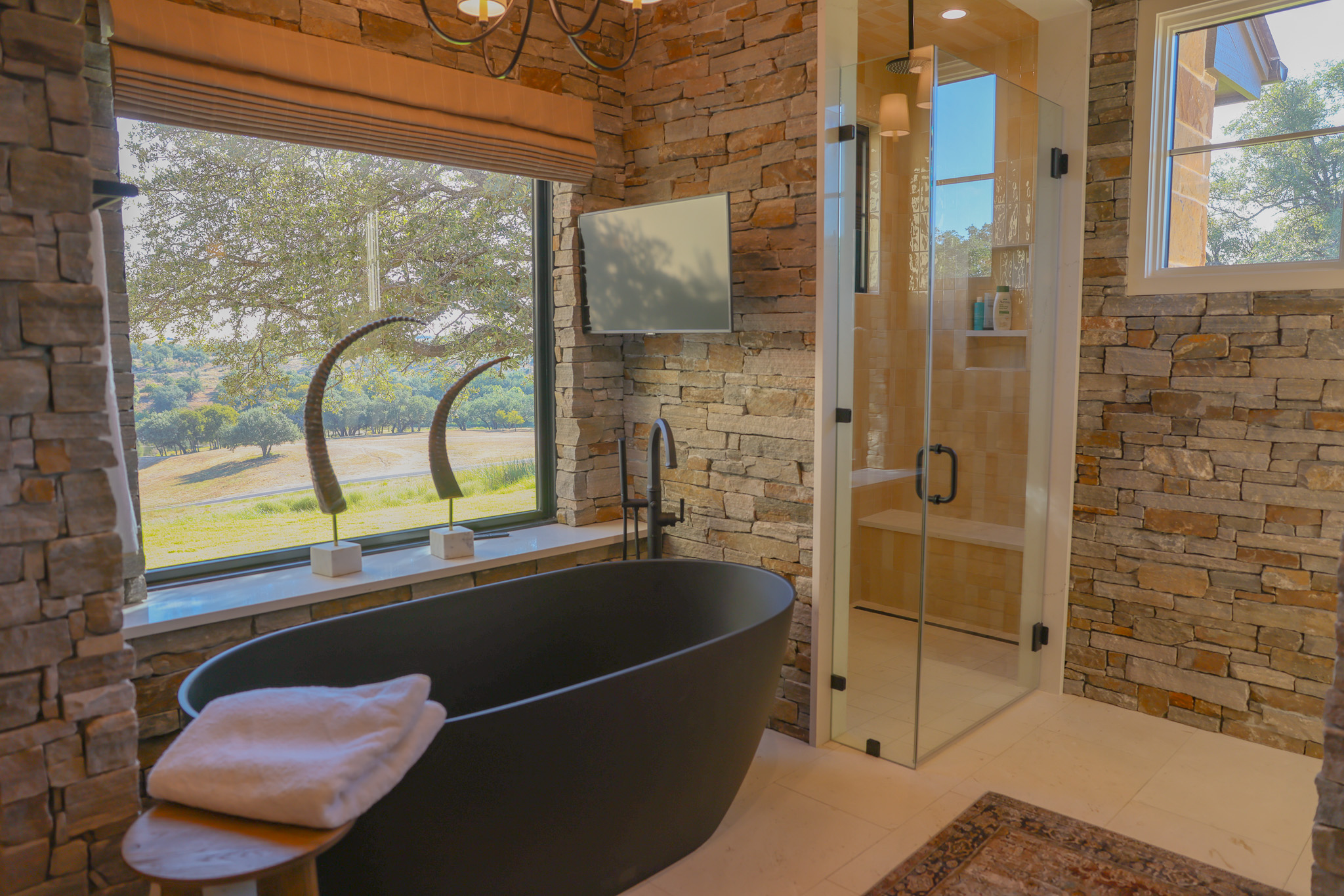 920 Ryan Road Bertram, TX 78605 - Photo 10 of 40 Natural stone walls frame a modern soaking tub alongside a glass-enclosed walk-in shower.
