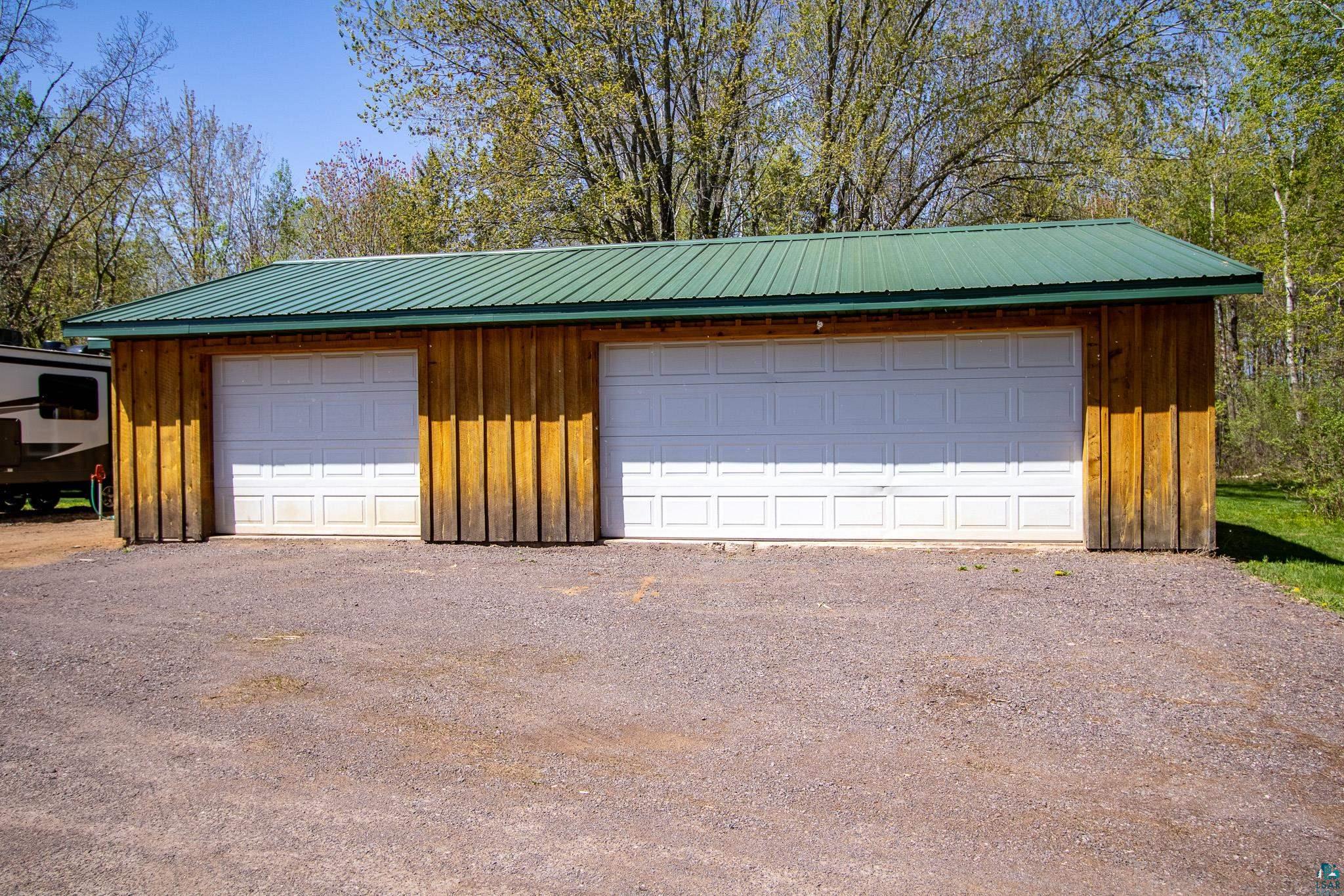37590 Degerstrom Road Askov, MN 55704 - Photo 35 of 53 Wood-sided detached garage featuring two white panel garage doors, a green metal roof, and a gravel driveway