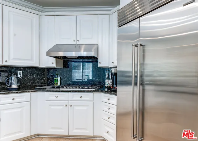 a kitchen with granite countertop a refrigerator and white cabinets