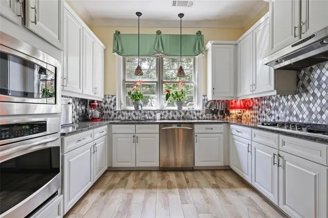 a kitchen with stainless steel appliances granite countertop a stove a sink and white cabinets