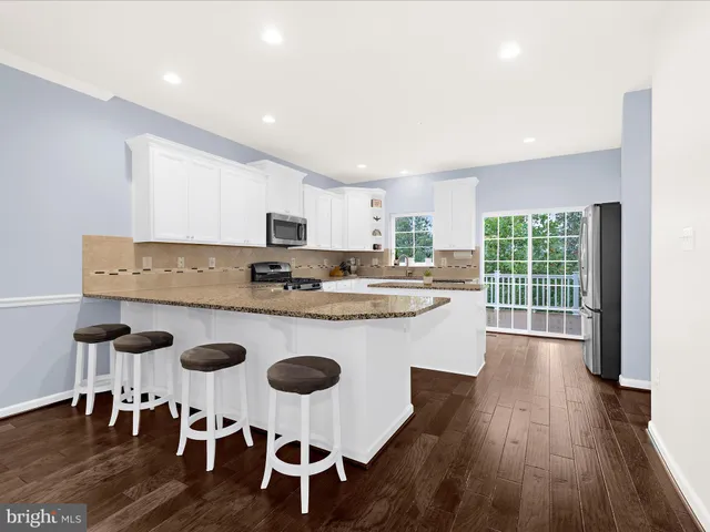 a kitchen with stainless steel appliances granite countertop a stove a refrigerator a kitchen island a dining table and chairs with wooden floor