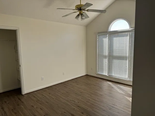 an empty room with wooden floor chandelier fan and windows