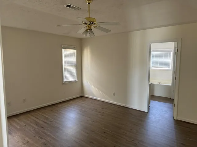 an empty room with wooden floor a ceiling fan and windows