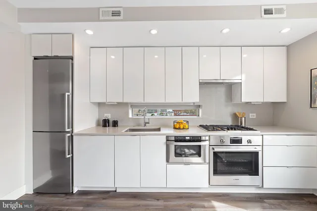 a kitchen with stainless steel appliances granite countertop a stove a refrigerator and a sink with white cabinets