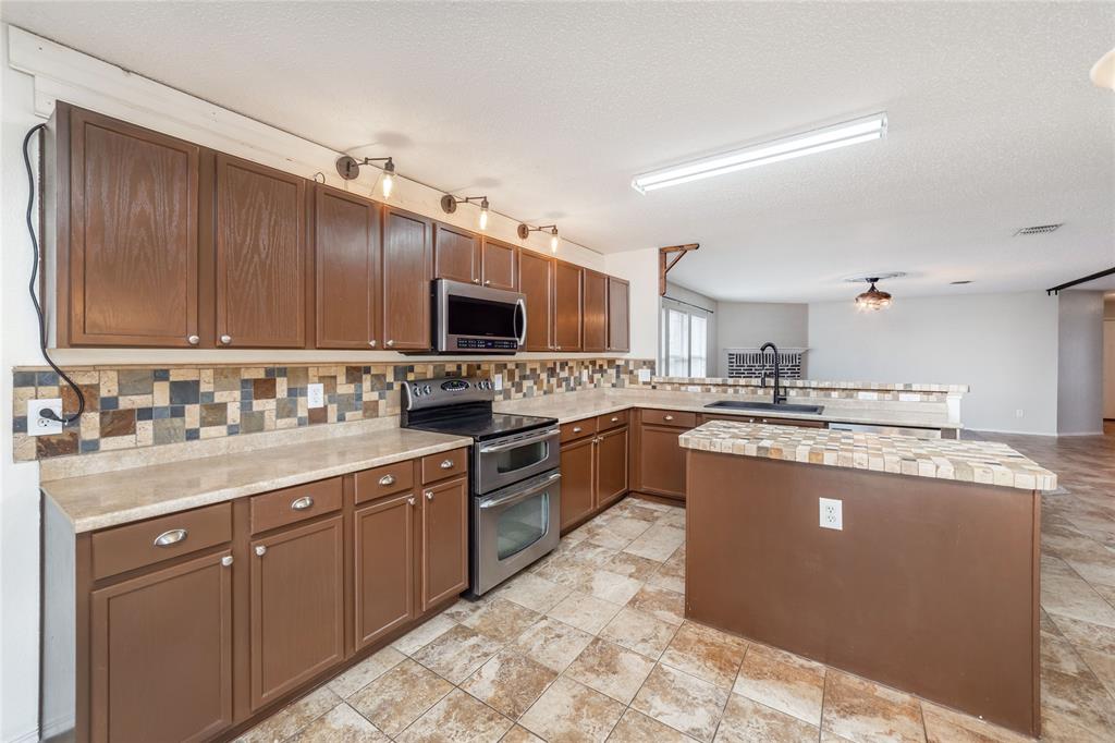 4408 Statesman Lane Fort Worth, TX 76244 - Photo 13 of 40 Kitchen with sink, kitchen peninsula, a textured ceiling, stainless steel appliances, and decorative backsplash