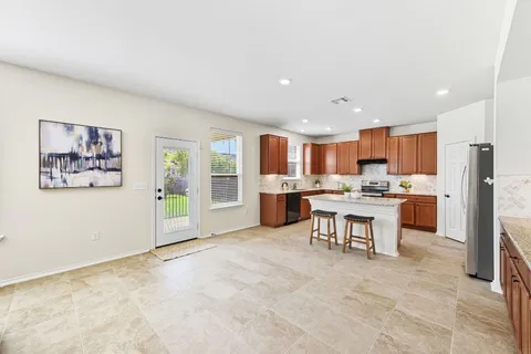 a kitchen with stainless steel appliances granite countertop a refrigerator a sink a stove a dining table and chairs