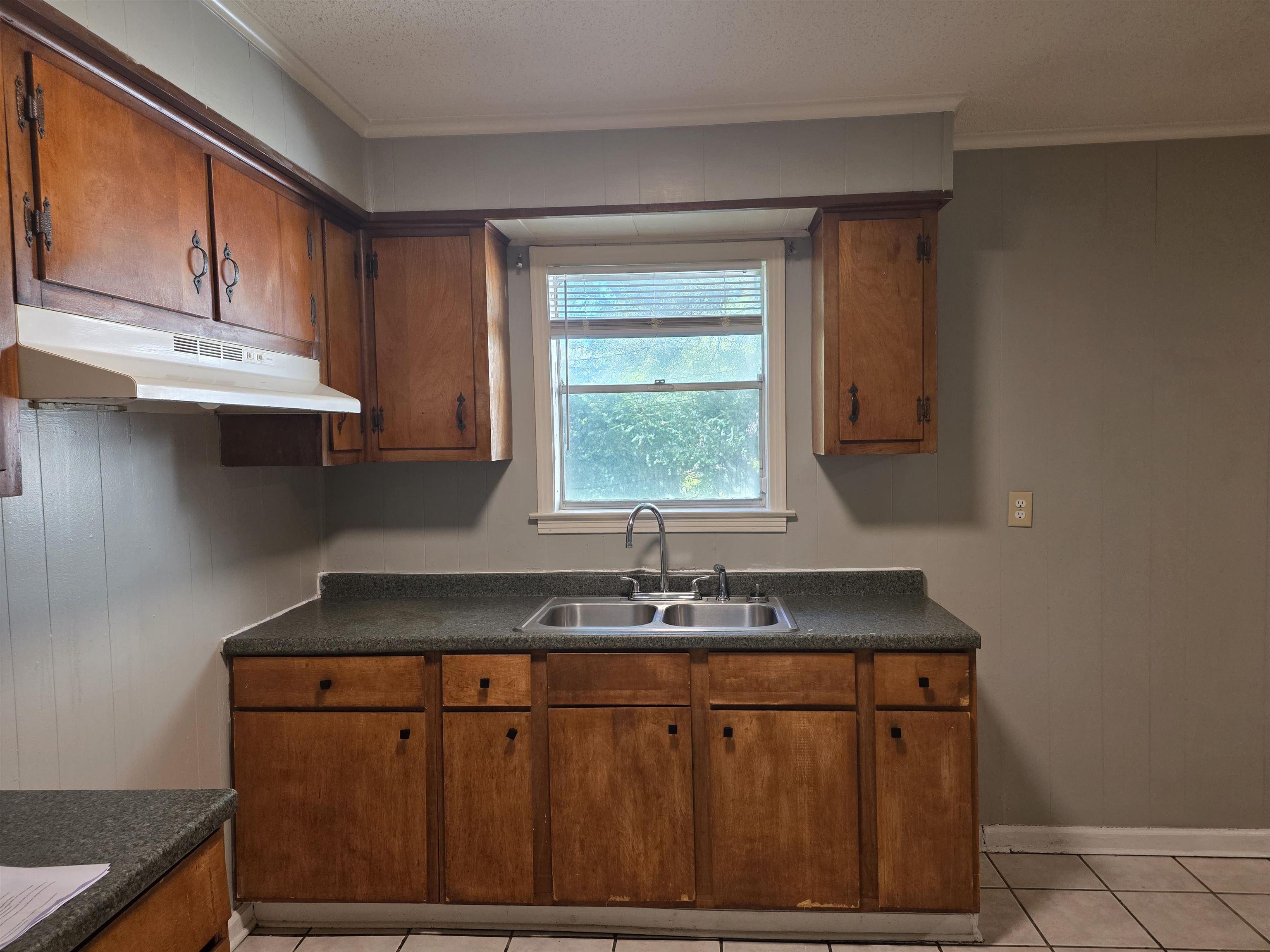 4573 Appleville Street Memphis, TN 38109 - Photo 11 of 22 Kitchen with dark countertops, light tile patterned floors, ornamental molding, under cabinet range hood, and brown cabinetry
