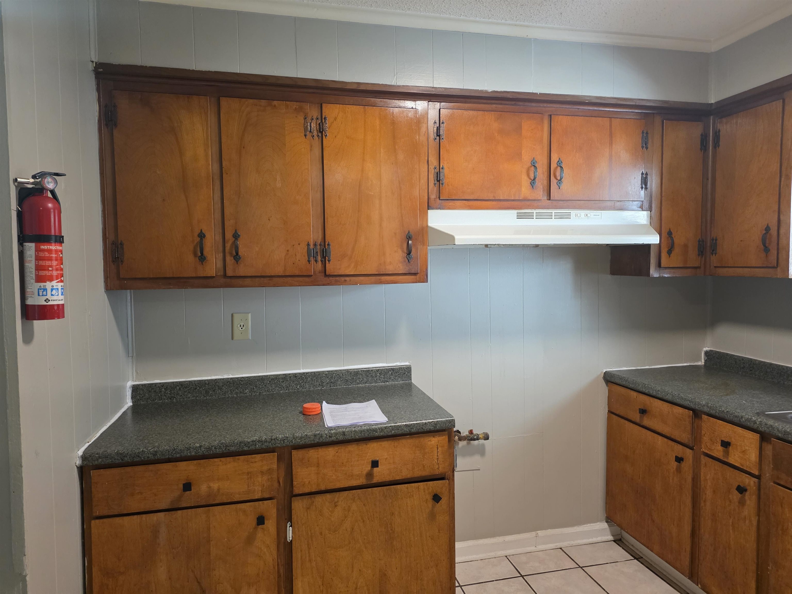 4573 Appleville Street Memphis, TN 38109 - Photo 12 of 22 Kitchen with brown cabinetry, dark countertops, light tile patterned floors, under cabinet range hood, and crown molding