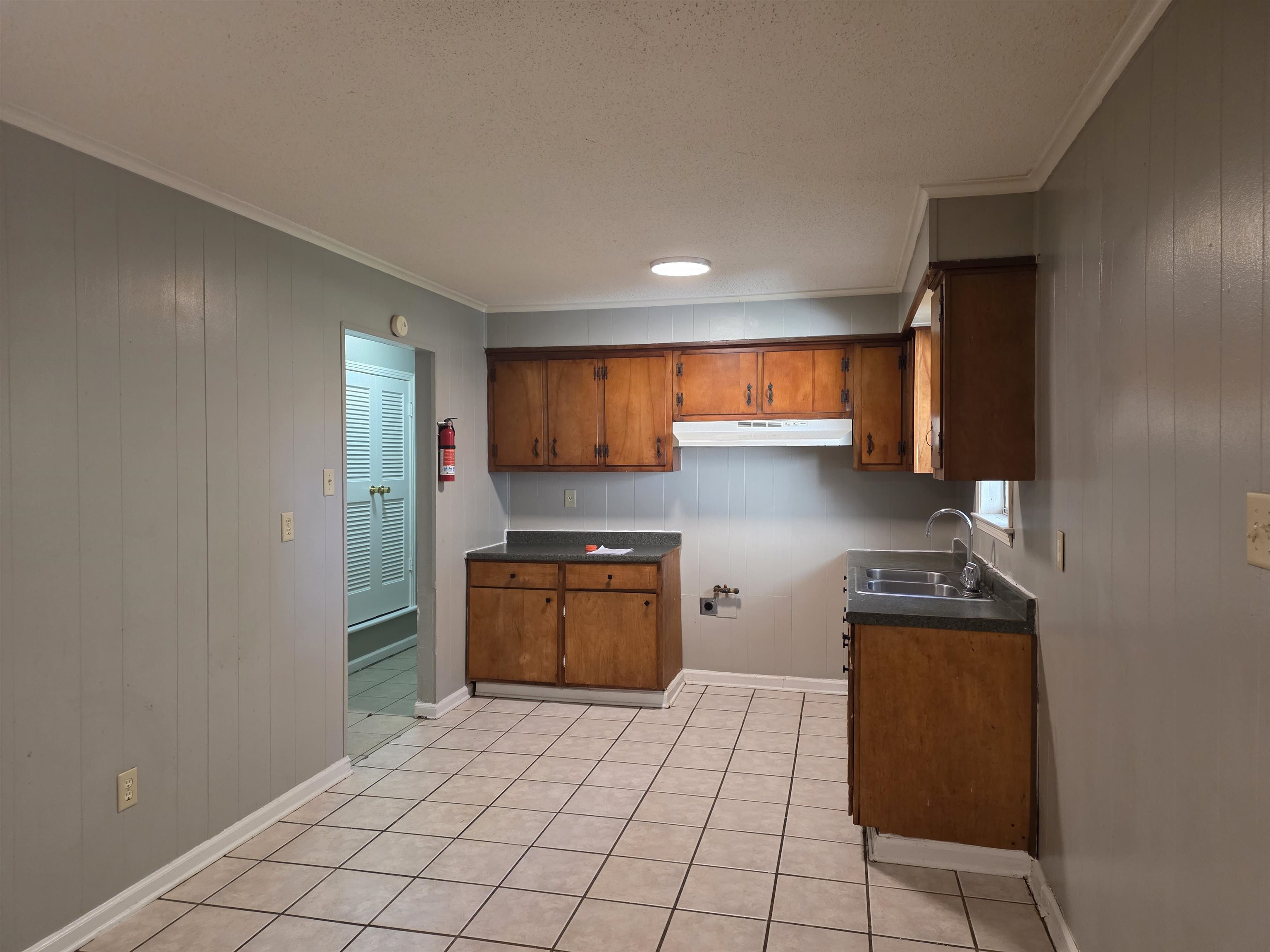 4573 Appleville Street Memphis, TN 38109 - Photo 13 of 22 Kitchen featuring wooden walls, dark countertops, brown cabinets, crown molding, and light tile patterned floors