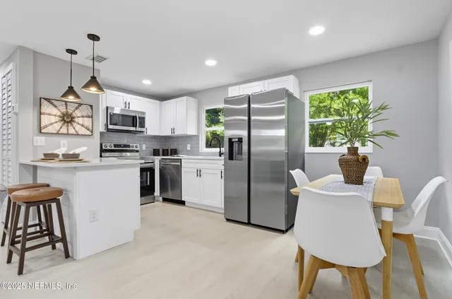 a kitchen with stainless steel appliances granite countertop a refrigerator a sink a stove a dining table and chairs