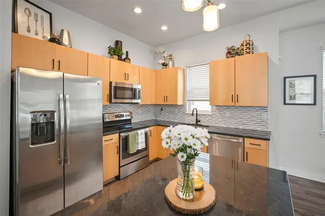 a kitchen with stainless steel appliances granite countertop a refrigerator a stove a sink and a dining table with wooden floor