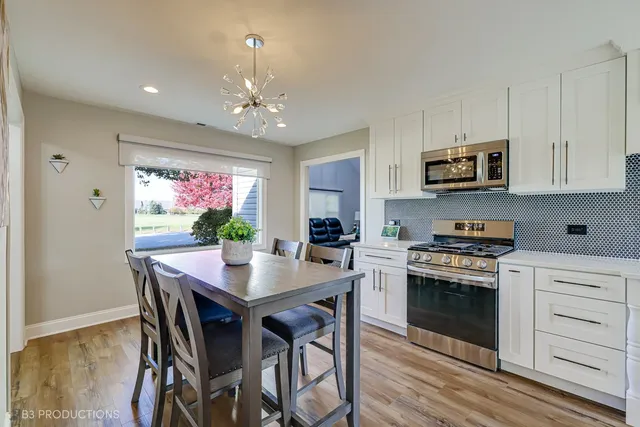 a kitchen with stainless steel appliances granite countertop a stove top oven a refrigerator a dining table and chairs with wooden floor