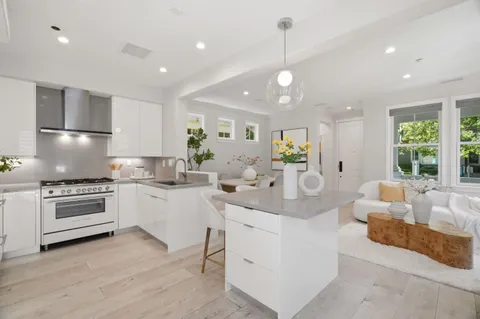 a large white kitchen with kitchen island a large counter space a sink stainless steel appliances and windows
