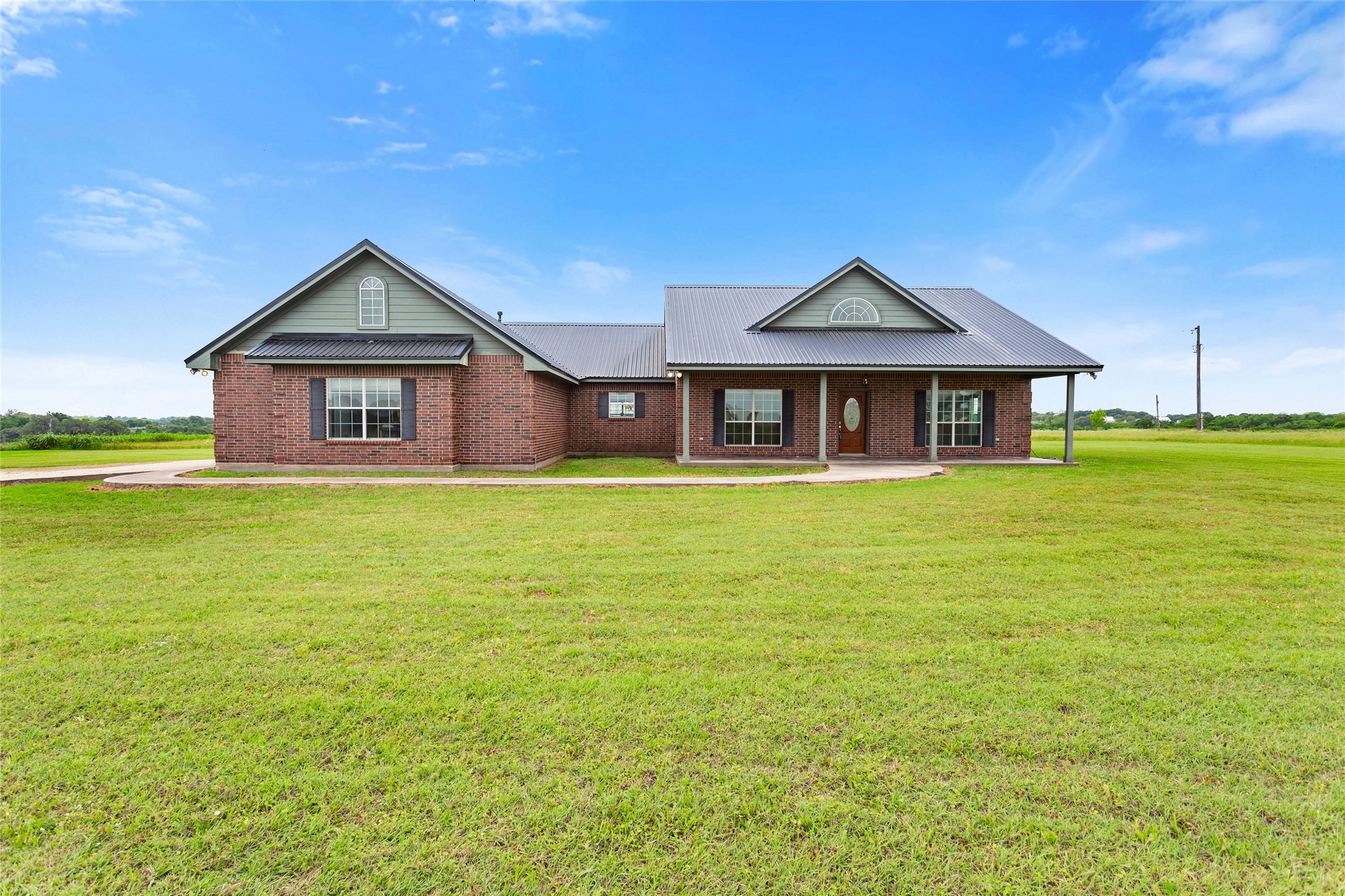 5750 Cedar Hill Road Brenham, TX 77833 - Photo 9 of 46 The image captures the front facade, emphasizing the generous size of the porch. Key architectural details visible are the soaring high ceilings and the sharply defined roof peaks. Large storage space in attic.