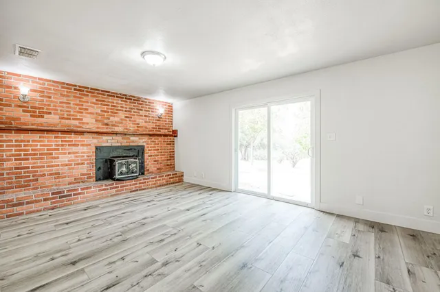 an empty room with wooden floor fireplace and windows