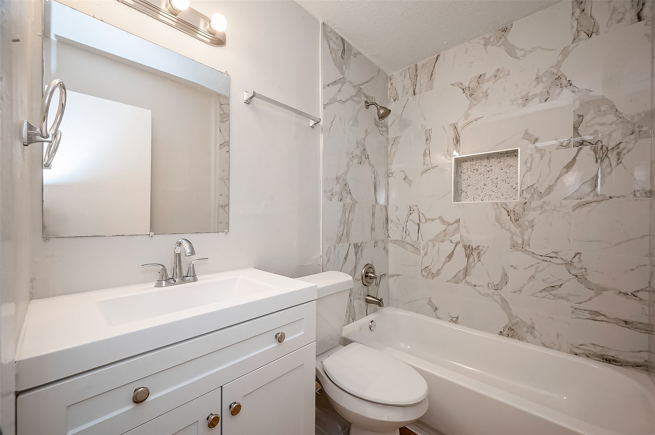 8814 Manus Street, Unit 5 Houston, TX 77093 - Photo 12 of 27 This bathroom features a modern design with elegant marble-patterned tiles, a sleek vanity with a mirror, and a shower-tub combination. Bright lighting and a clean aesthetic create a fresh, inviting space.