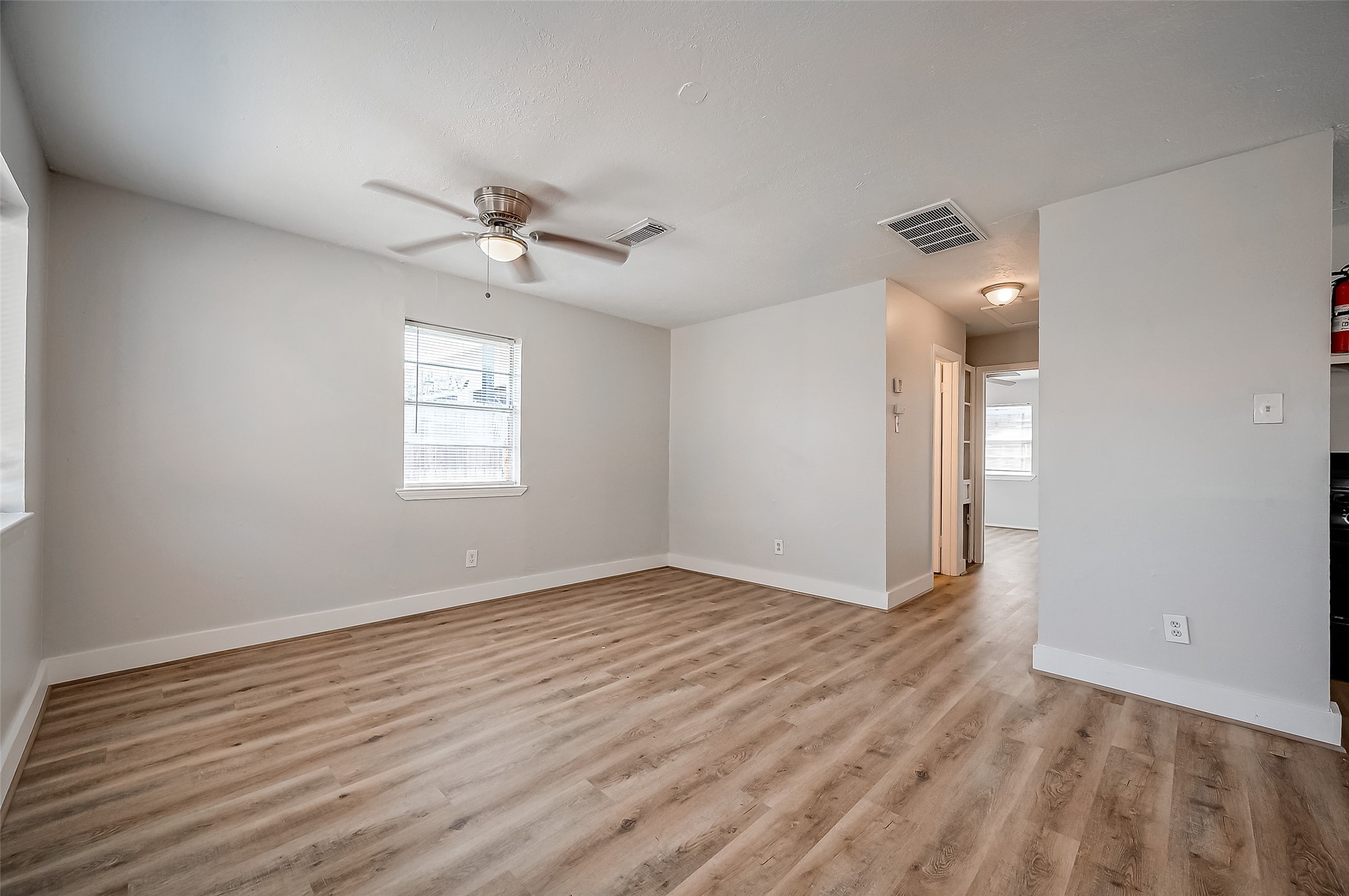 8814 Manus Street, Unit 5 Houston, TX 77093 - Photo 13 of 27 Bright and airy room with light wood flooring, neutral walls, and a ceiling fan. It features ample natural light from two windows and has an adjacent hallway leading to other areas of the home.