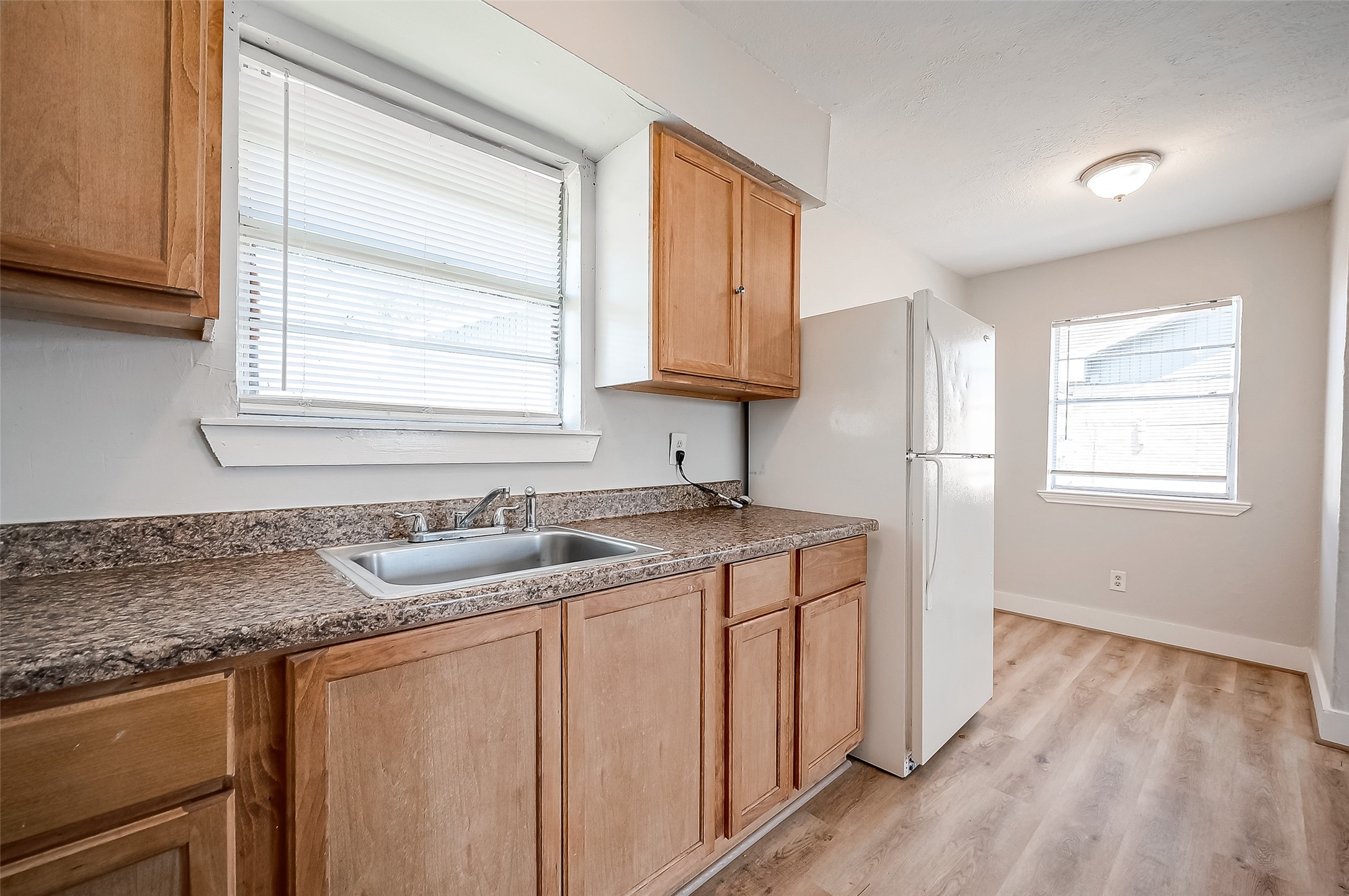 8814 Manus Street, Unit 5 Houston, TX 77093 - Photo 22 of 27 Bright kitchen with natural light, featuring wooden cabinets, granite countertops, and laminate wood flooring. Includes a sink with a window view and a white refrigerator.