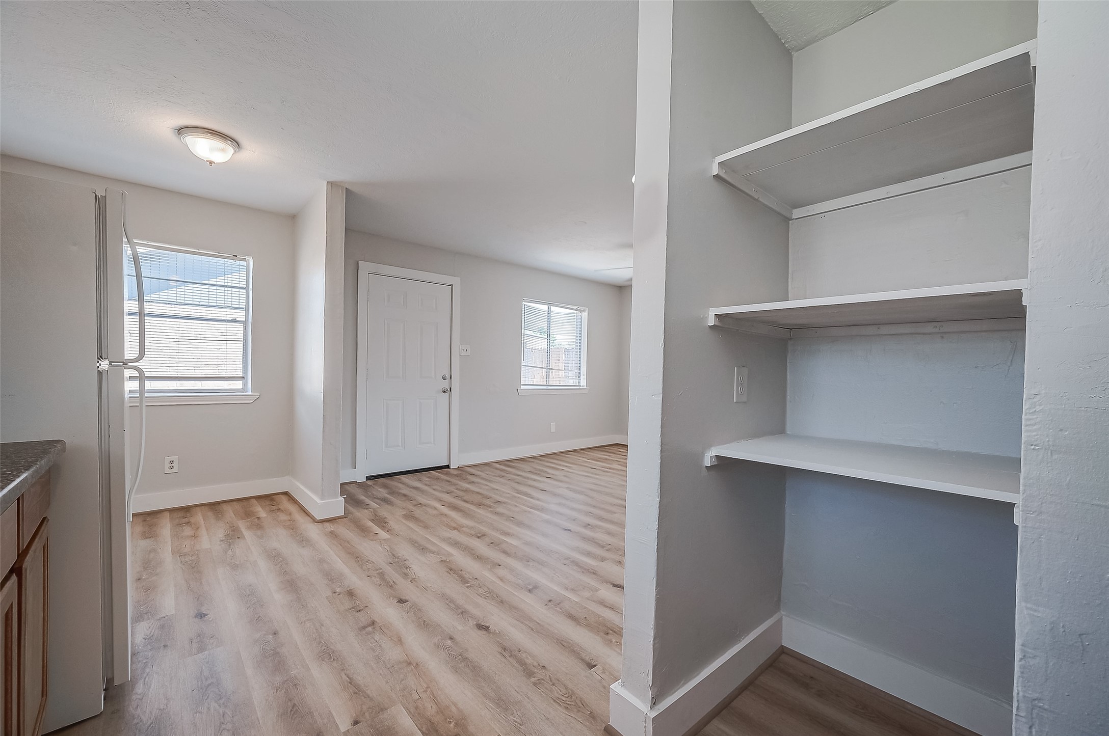 8814 Manus Street, Unit 5 Houston, TX 77093 - Photo 23 of 27 This photo showcases a bright, open living area with light wood flooring, neutral walls, and ample natural light. The room has built-in shelving and a view of the kitchen, featuring modern appliances and a clean design.