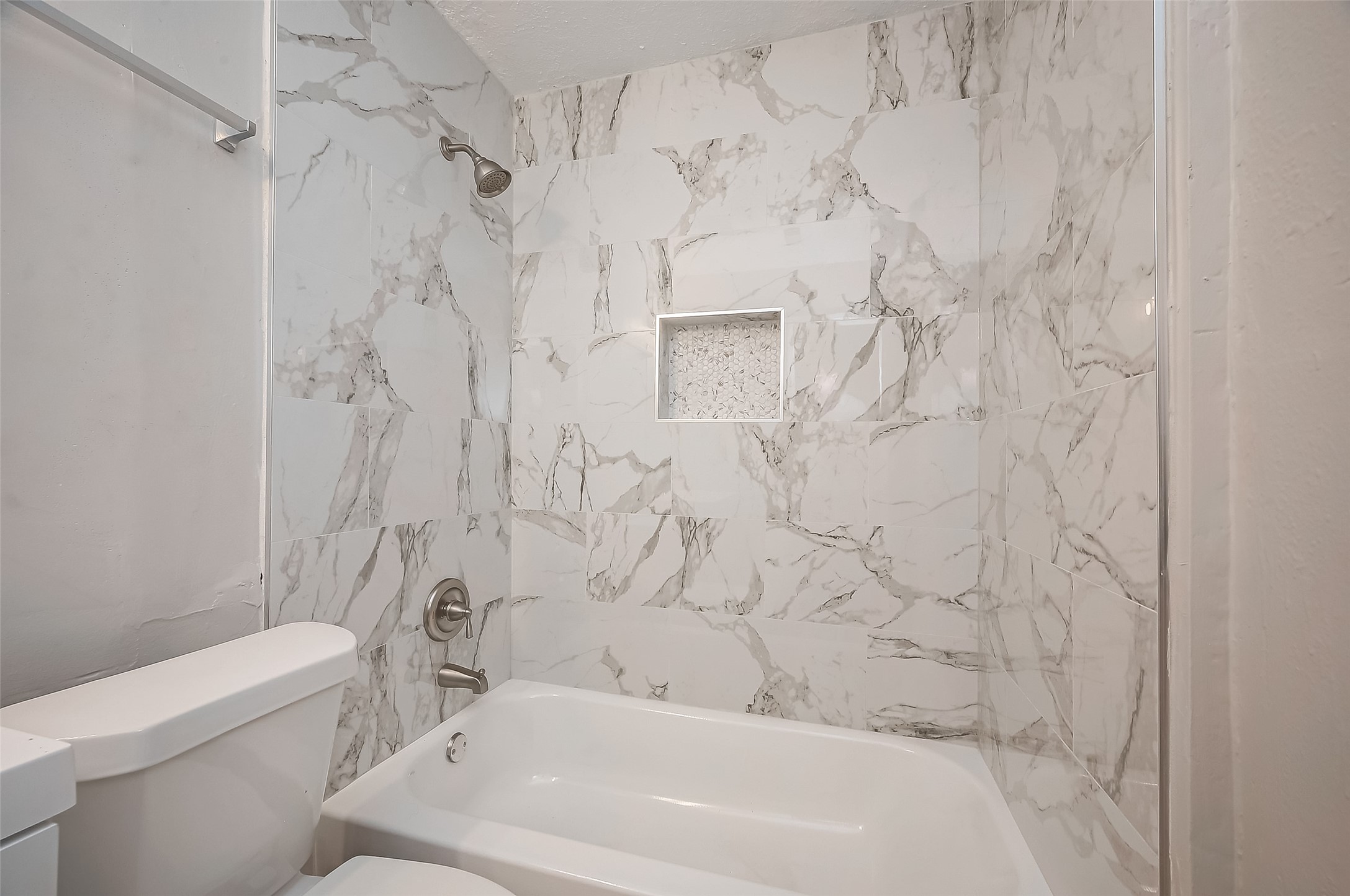 8814 Manus Street, Unit 5 Houston, TX 77093 - Photo 25 of 27 This bathroom features a modern bathtub and shower combo with elegant marble-patterned tiles, complemented by brushed nickel fixtures and a convenient built-in shower niche.