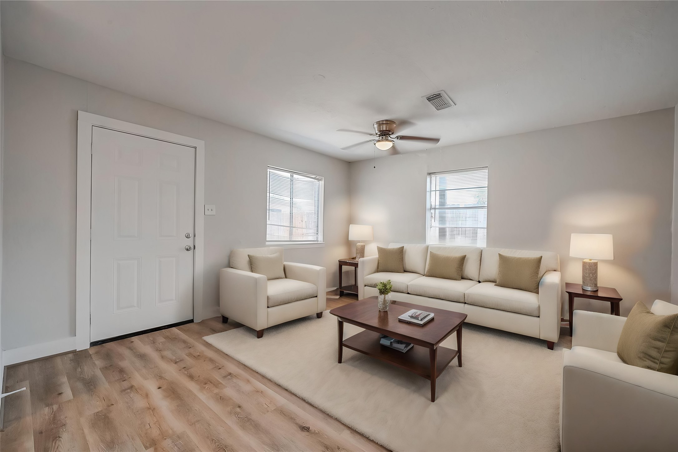 8814 Manus Street, Unit 5 Houston, TX 77093 - Photo 10 of 27 Bright and inviting living room with neutral tones, featuring comfortable seating, a ceiling fan, and ample natural light from two windows. The space is complemented by a warm wood floor and stylish decor.