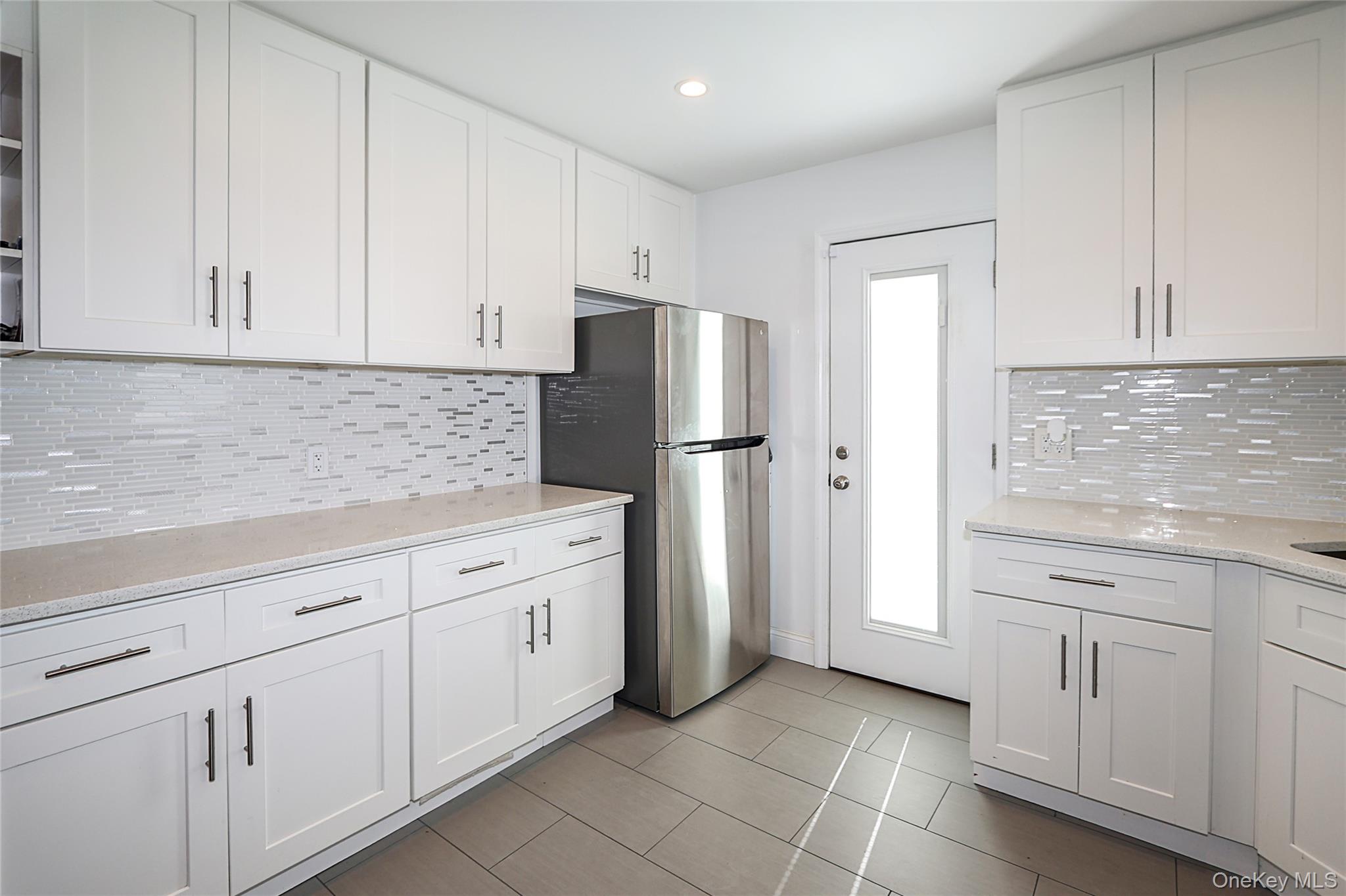 132 Bethel Road Albertson, NY 11507 - Photo 5 of 28 Kitchen featuring white cabinets, tasteful backsplash, light stone counters, freestanding refrigerator, and recessed lighting