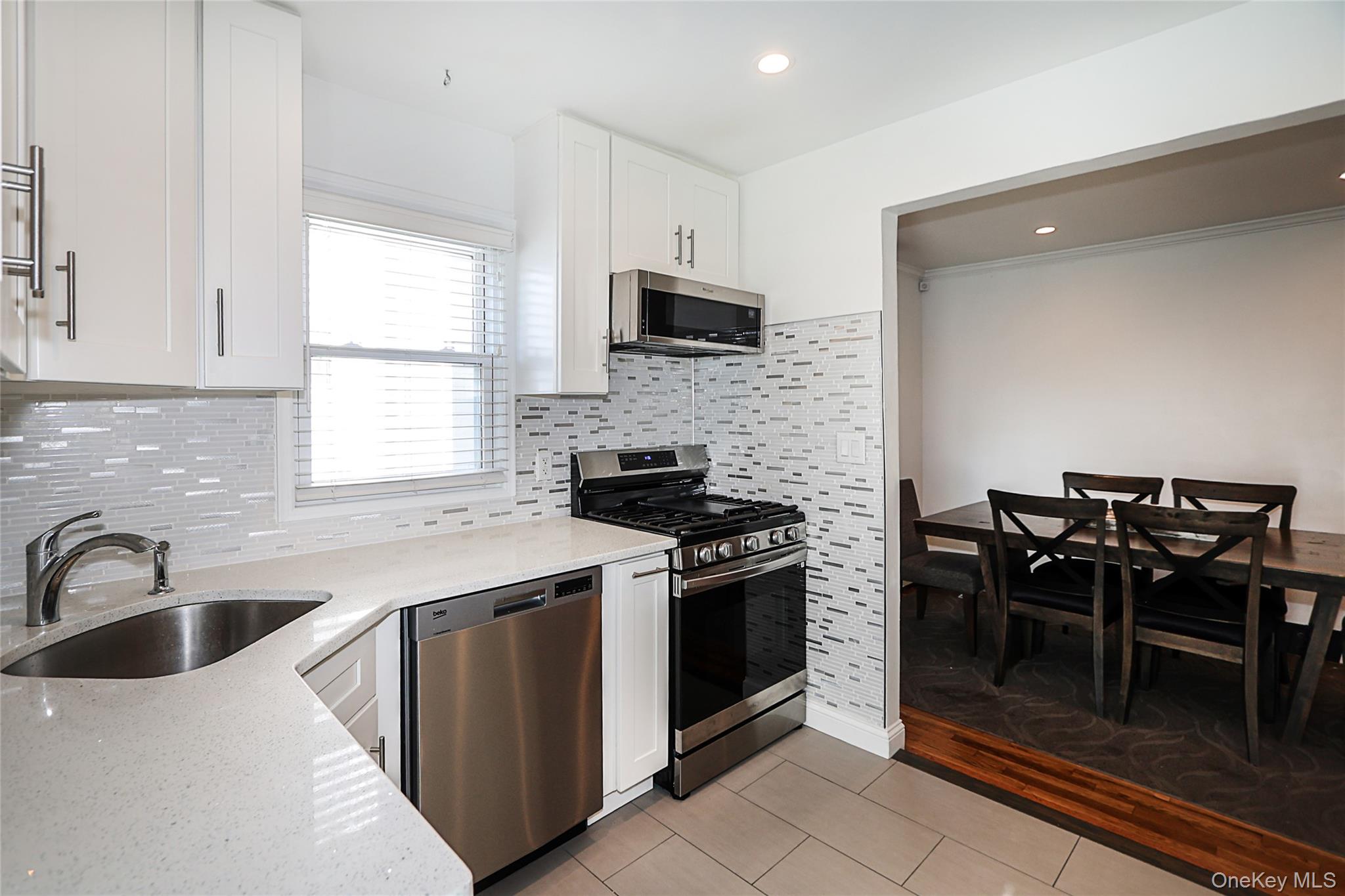 132 Bethel Road Albertson, NY 11507 - Photo 7 of 28 Kitchen featuring light stone countertops, white cabinets, stainless steel appliances, tasteful backsplash, and light tile patterned floors