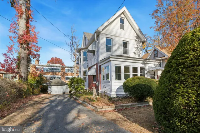 a view of a white house next to a yard with plants and trees