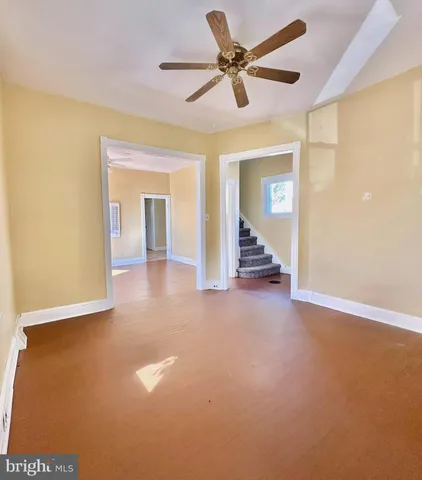 an empty room with fan and way to kitchen