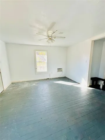 an empty room with wooden floor ceiling fan and windows