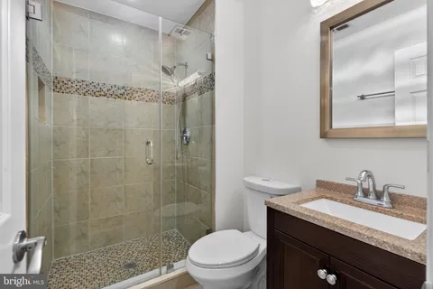 a bathroom with a granite countertop sink a toilet a mirror and shower