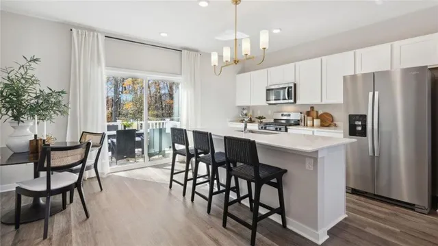 a kitchen with stainless steel appliances granite countertop a dining table chairs refrigerator and sink