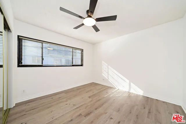an empty room with wooden floor fan and windows