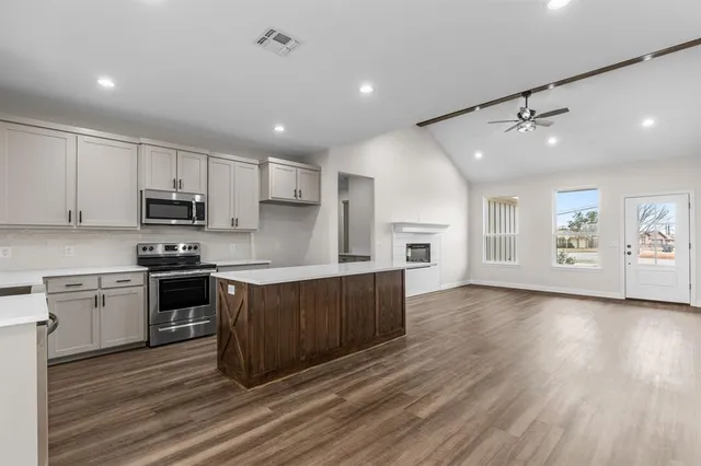 a large kitchen with stainless steel appliances granite countertop a stove a sink dishwasher and a refrigerator with wooden floor