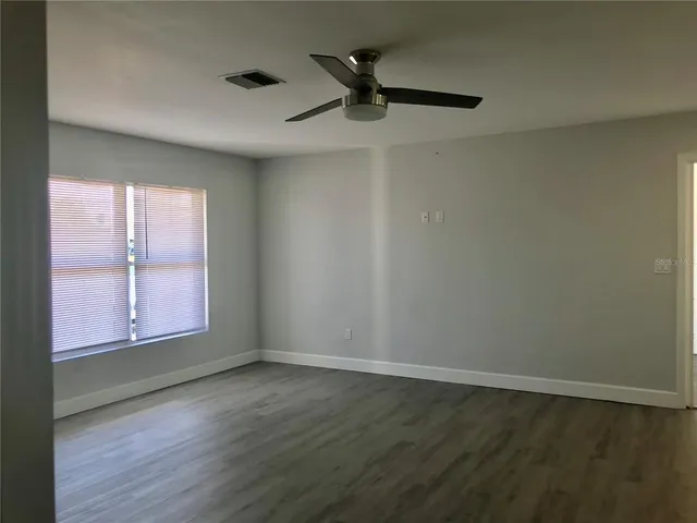 an empty room with wooden floor fan and windows