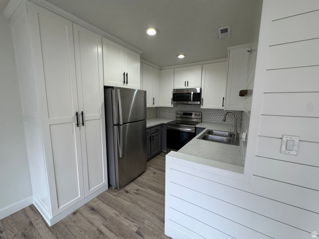 608 South 500 West, Unit 3 Provo, UT 84601 - Photo 12 of 35 Kitchen featuring white shaker cabinetry, stainless steel appliances, a honeycomb tile backsplash, wood-finish flooring, and shiplap paneling
