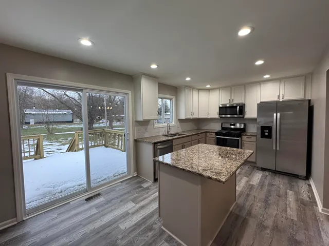 a kitchen with stainless steel appliances granite countertop a refrigerator a sink dishwasher a oven and a large island with wooden floor