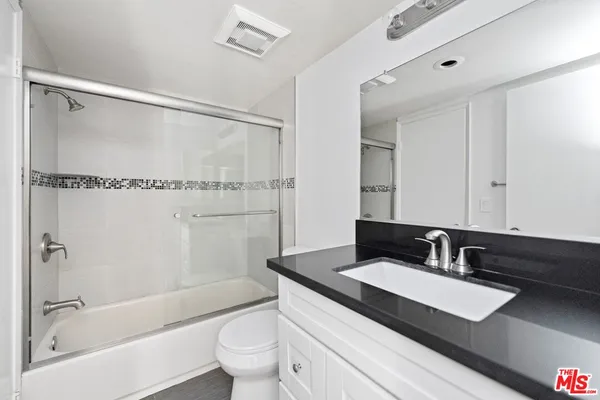 a bathroom with a granite countertop sink a toilet and shower