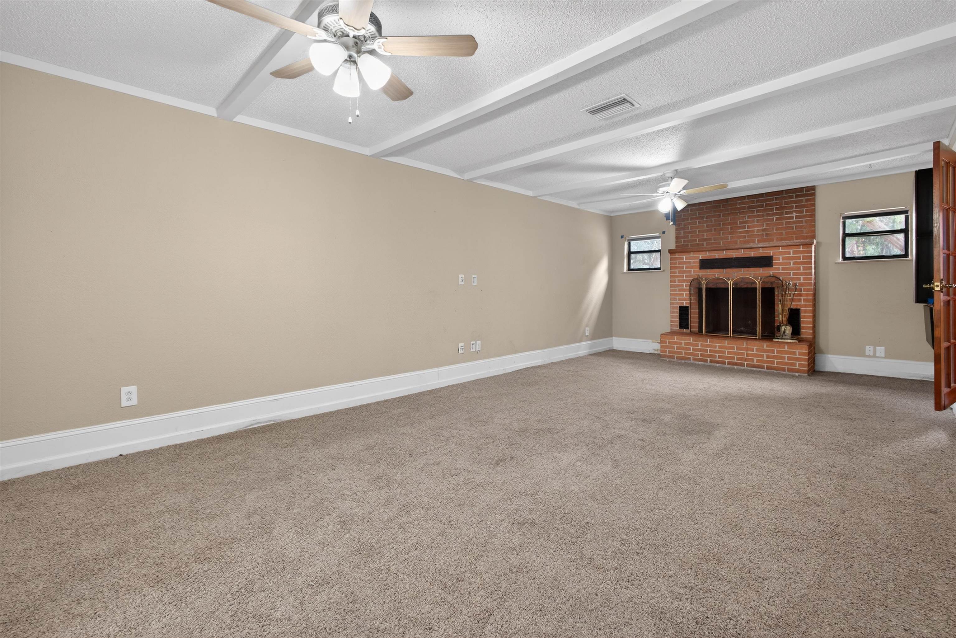 2907 North 5th Street St. Augustine, FL 32084 - Photo 40 of 71 Unfurnished living room with a brick fireplace, carpet flooring, a textured ceiling, beamed ceiling, and ceiling fan