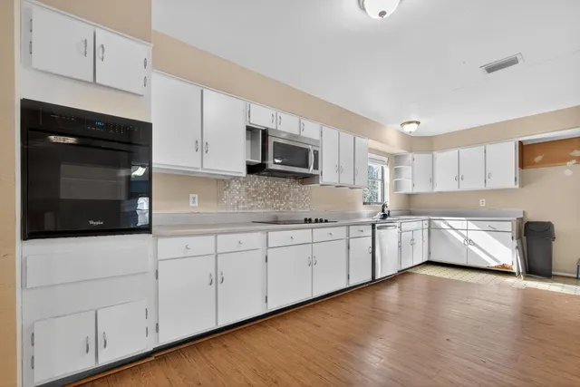 a view of a kitchen with stainless steel appliances granite countertop a stove a sink and white cabinets with wooden floor