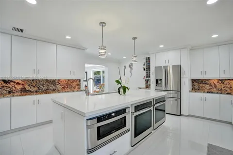 a large white kitchen with a stove a sink a refrigerator and a dining table with wooden floor