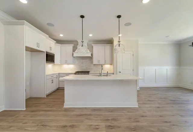 a large kitchen with stainless steel appliances a large counter top a sink a refrigerator and a chandelier