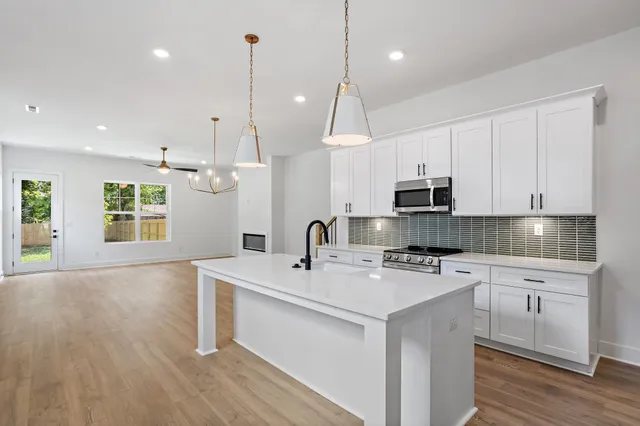 a kitchen with stainless steel appliances granite countertop a sink a stove a refrigerator and white cabinets with wooden floor