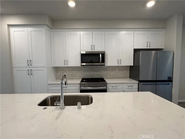 a kitchen with stainless steel appliances granite countertop a refrigerator a stove a sink and white cabinets