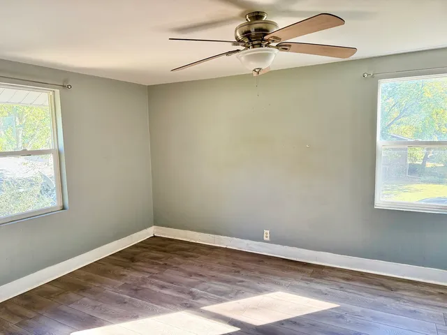 an empty room with wooden floor fan and windows