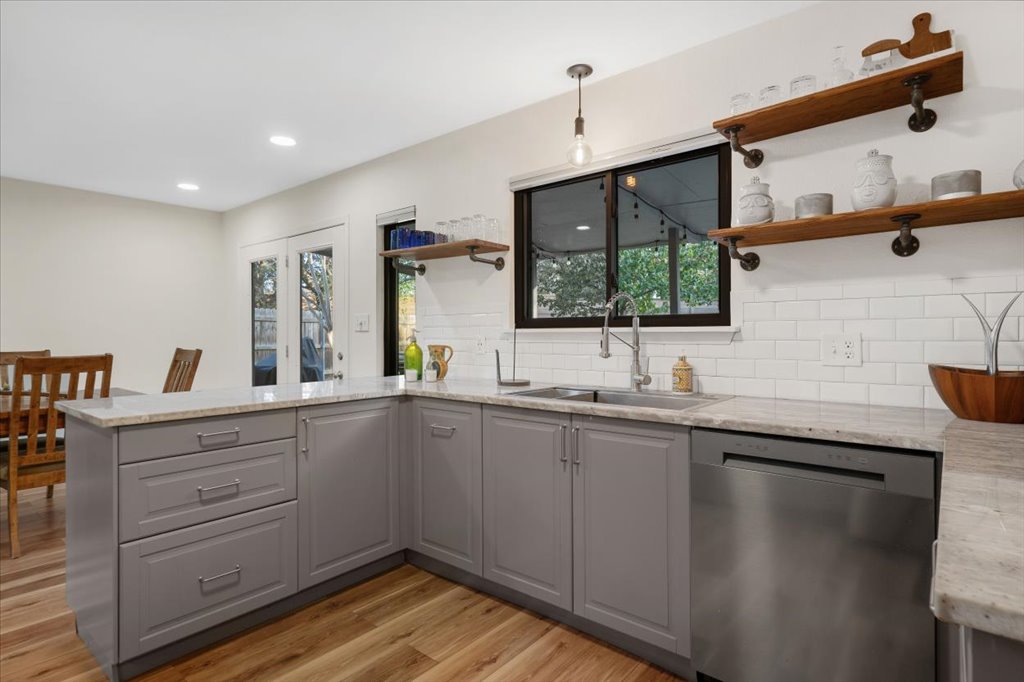 13126 Travis View Loop Austin, TX 78732 - Photo 8 of 27 Kitchen with stainless steel dishwasher, gray cabinets, a peninsula, open shelves, and light stone counters