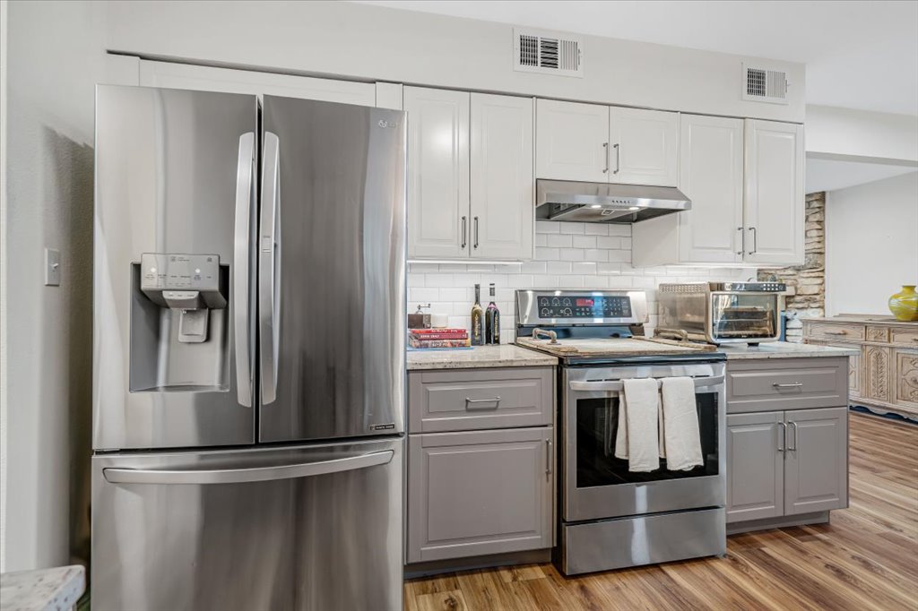13126 Travis View Loop Austin, TX 78732 - Photo 9 of 27 Kitchen featuring stainless steel appliances, gray cabinets, light wood-style flooring, and decorative backsplash