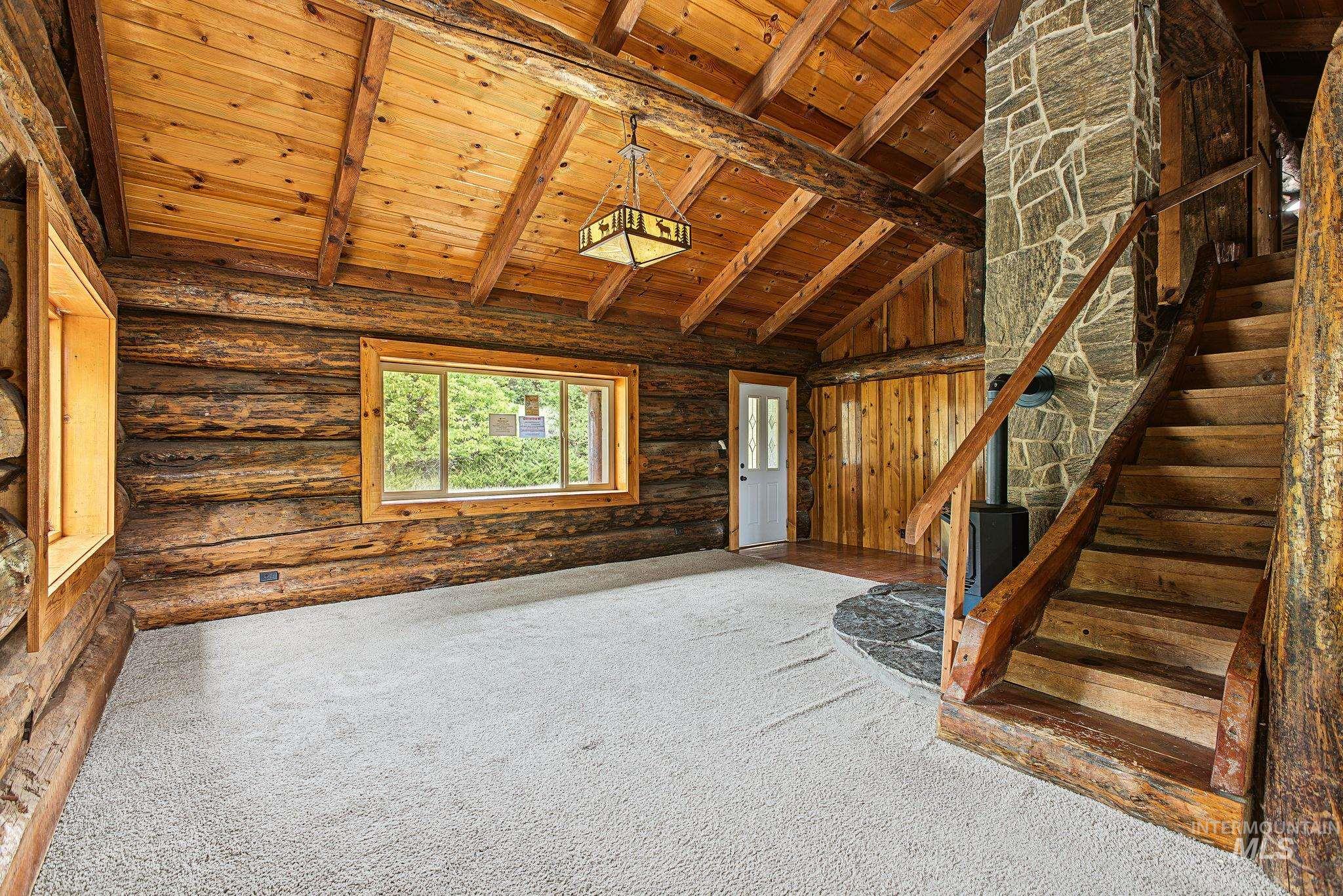 Vaulted wood-paneled ceiling with exposed beams, wood-plank walls, natural stone fireplace, and wood staircase with railing