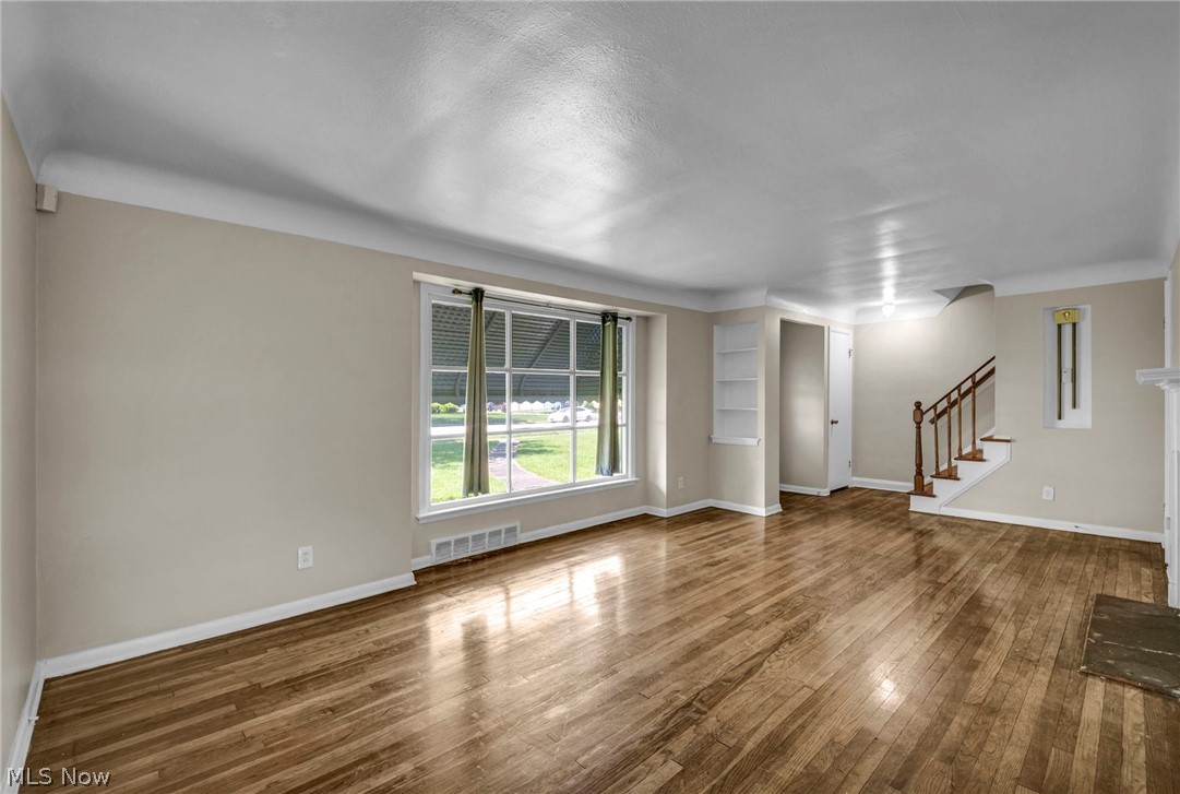 2313 North Taylor Road Cleveland Heights, OH 44112 - Photo 6 of 32 Spacious room featuring wood-finish flooring, a large multi-pane window, built-in shelving, a staircase with wooden handrails, and a fireplace with a stone hearth